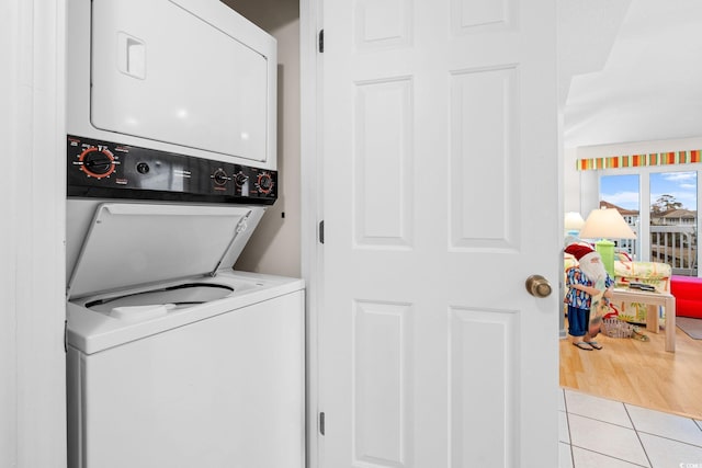 laundry area with stacked washer / drying machine and light tile patterned floors