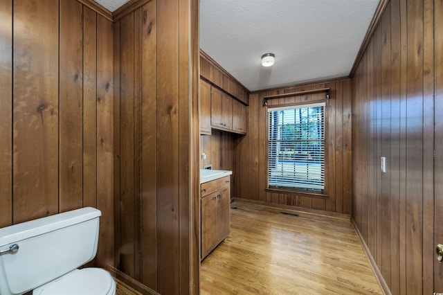 bathroom with a textured ceiling, wooden walls, wood finished floors, and toilet