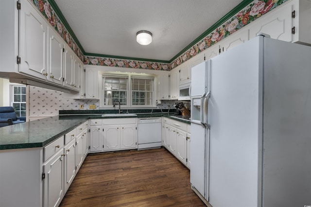 kitchen with a sink, white appliances, dark countertops, and a wealth of natural light