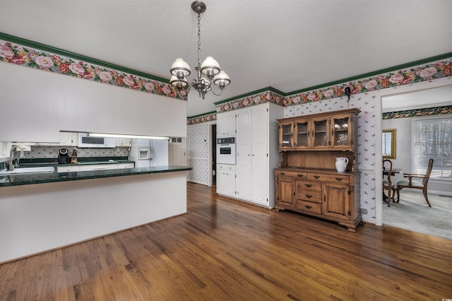 kitchen with dark wood-type flooring, a sink, dark countertops, white appliances, and a chandelier