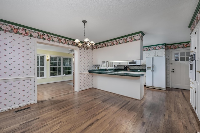 kitchen featuring visible vents, white appliances, a peninsula, an inviting chandelier, and wallpapered walls