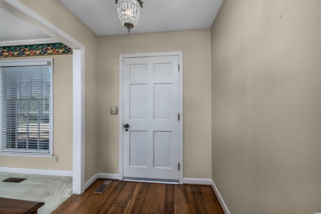 foyer entrance with an inviting chandelier, dark wood-style floors, visible vents, and baseboards