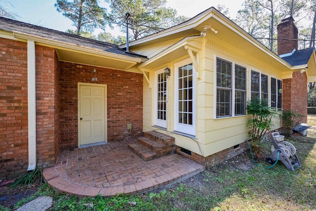 view of exterior entry with crawl space, a patio area, a chimney, and brick siding