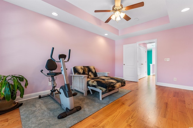 workout area with ceiling fan, hardwood / wood-style flooring, and a tray ceiling