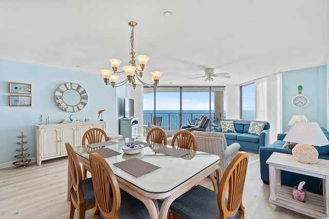 dining space with floor to ceiling windows, ceiling fan with notable chandelier, and light wood-type flooring