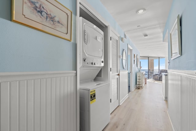 washroom with stacked washing maching and dryer and light hardwood / wood-style flooring