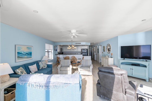 living room featuring ceiling fan with notable chandelier and light hardwood / wood-style flooring