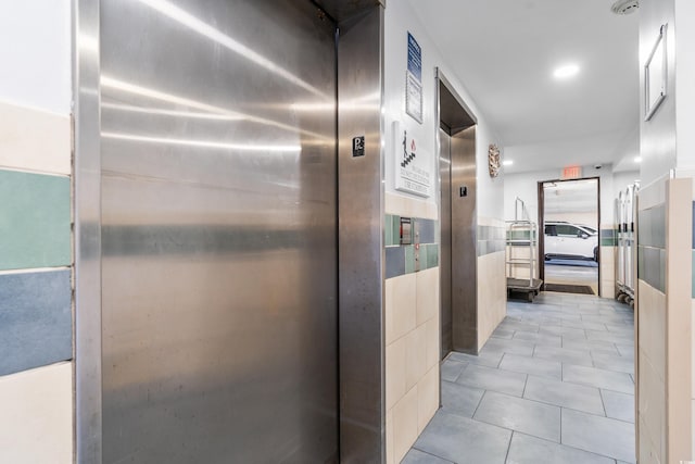 hallway with light tile patterned flooring, elevator, and tile walls