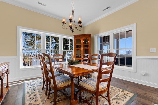 dining area with dark wood-type flooring, ornamental molding, and a chandelier