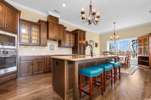 kitchen with built in microwave, oven, a chandelier, hanging light fixtures, and a center island with sink