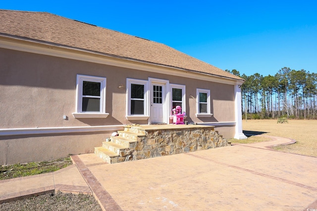 rear view of property featuring a patio area, stucco siding, and roof with shingles