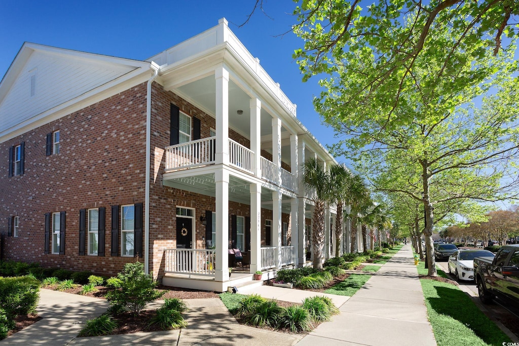 exterior space with covered porch, brick siding, and a balcony