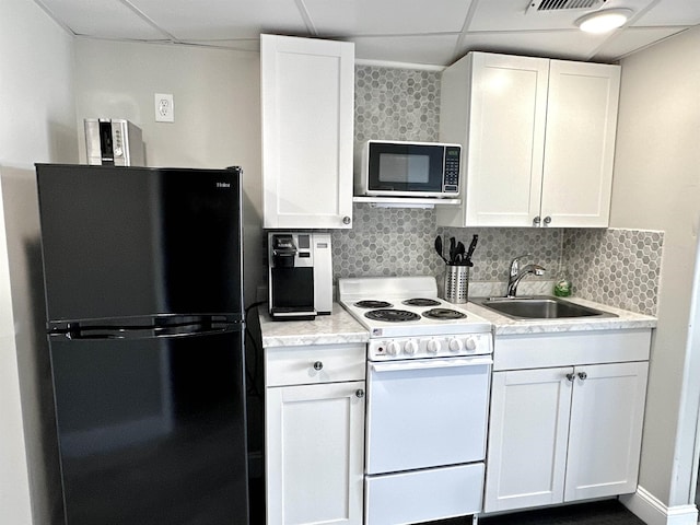 kitchen featuring white electric range oven, white cabinetry, black fridge, and a drop ceiling