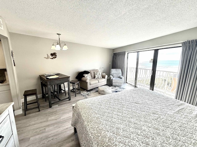 bedroom with a water view, a textured ceiling, access to exterior, a notable chandelier, and light hardwood / wood-style floors