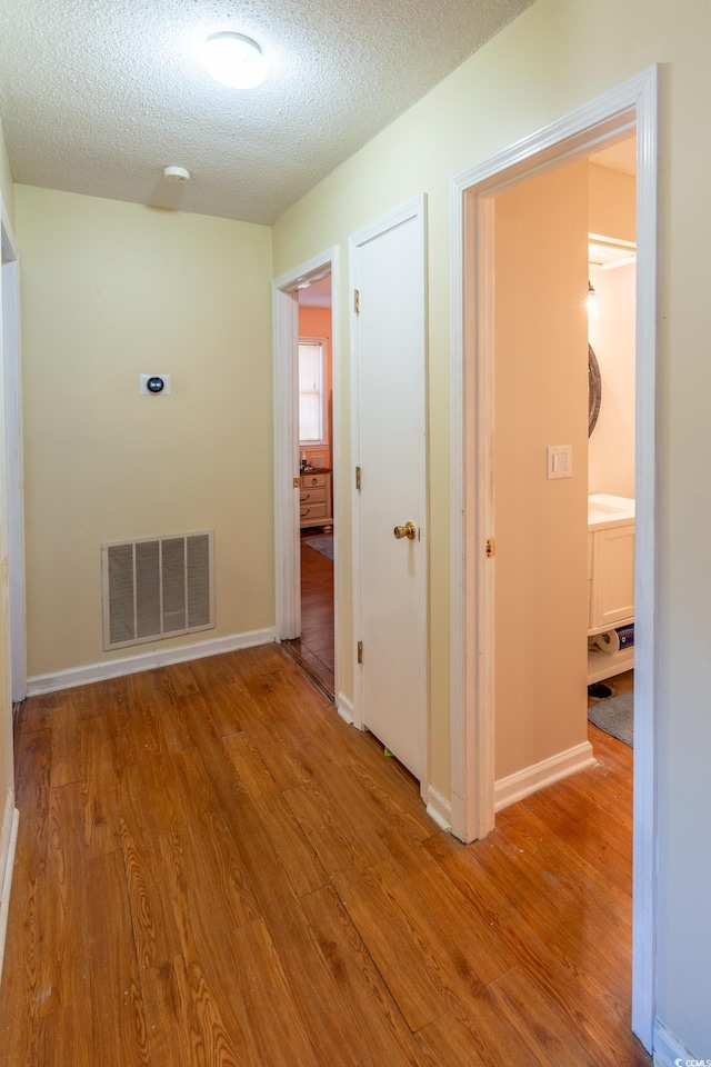 hall with light hardwood / wood-style floors and a textured ceiling