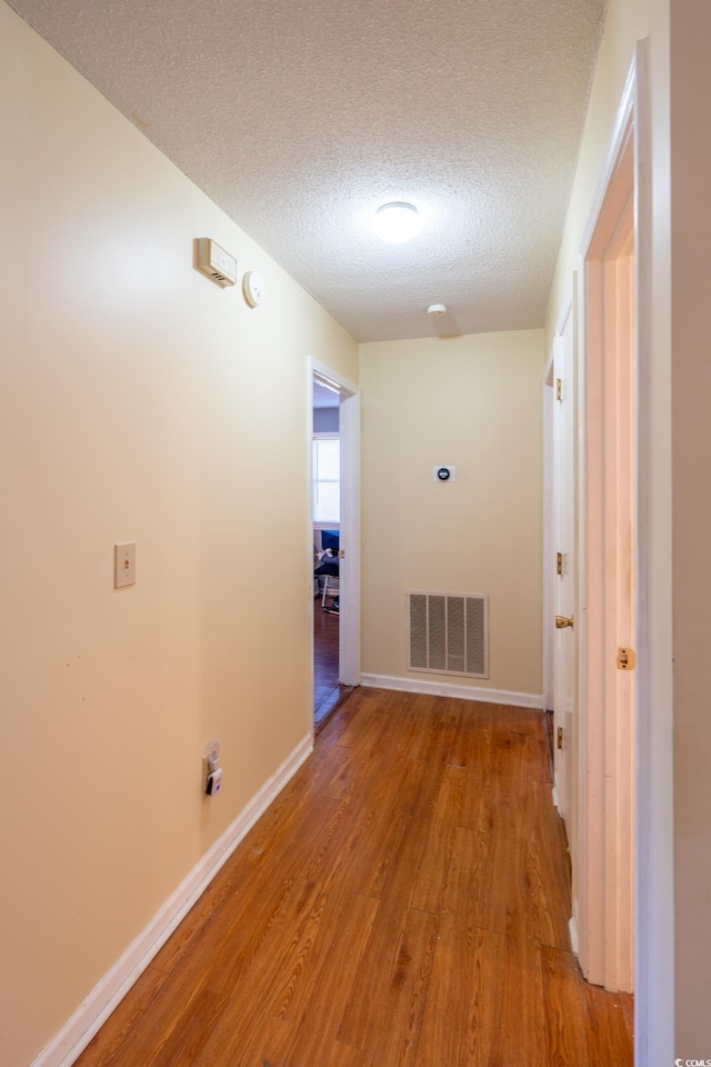 hall with a textured ceiling and light wood-type flooring