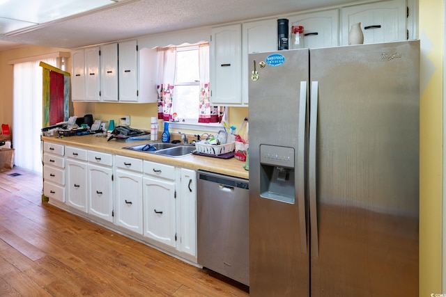 kitchen featuring sink, white cabinetry, a textured ceiling, light wood-type flooring, and appliances with stainless steel finishes