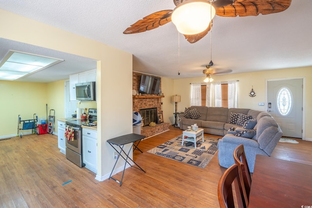 living room featuring ceiling fan, a textured ceiling, a fireplace, and light wood-type flooring