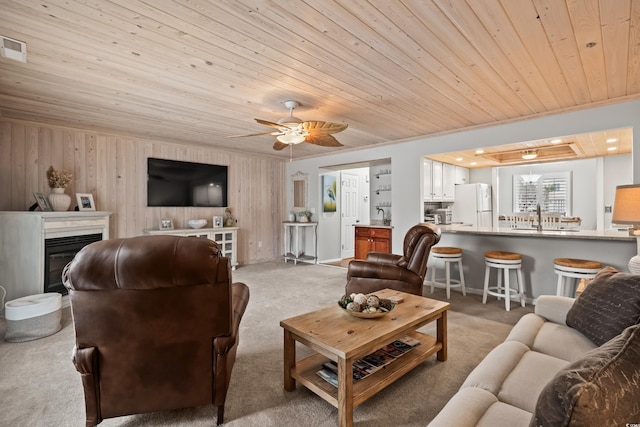 living room featuring ceiling fan, wooden ceiling, light colored carpet, and wooden walls