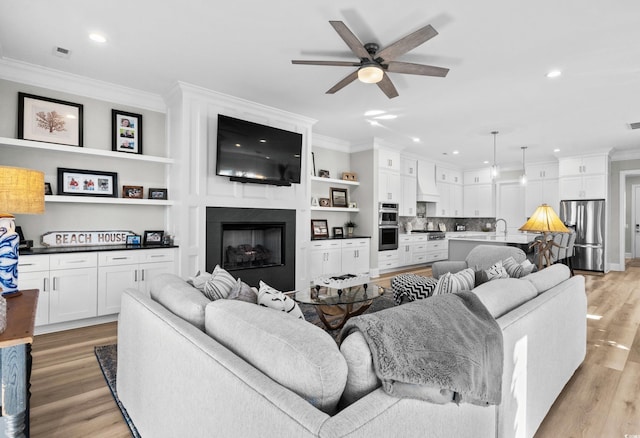 living room featuring ornamental molding, sink, ceiling fan, and light wood-type flooring