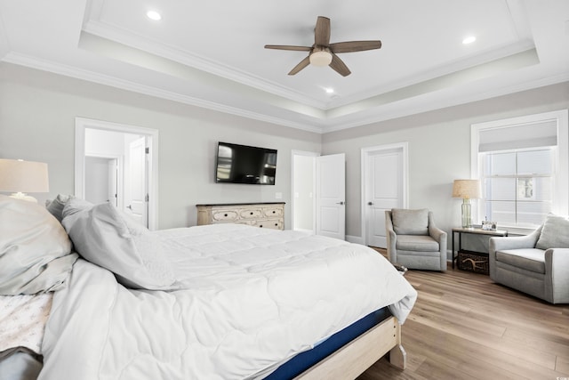 bedroom featuring crown molding, light hardwood / wood-style flooring, ceiling fan, and a tray ceiling