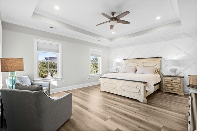 bedroom with a tray ceiling, ornamental molding, ceiling fan, and light wood-type flooring