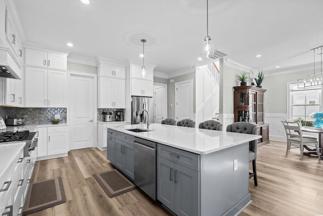 kitchen with gray cabinets, appliances with stainless steel finishes, white cabinetry, a kitchen island with sink, and a kitchen breakfast bar