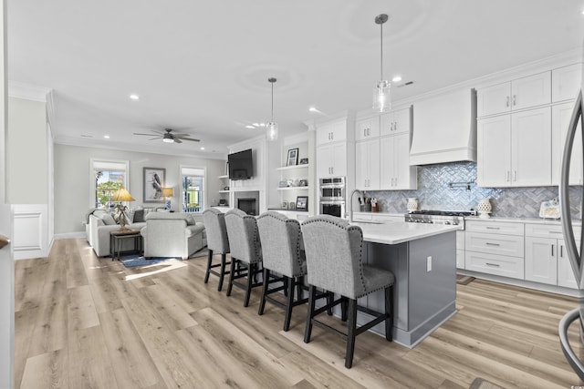 kitchen with a kitchen island with sink, hanging light fixtures, custom range hood, and white cabinets