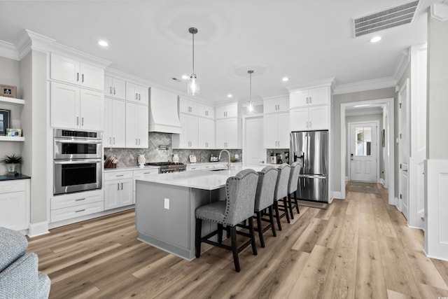 kitchen featuring custom exhaust hood, stainless steel appliances, a breakfast bar area, and white cabinets