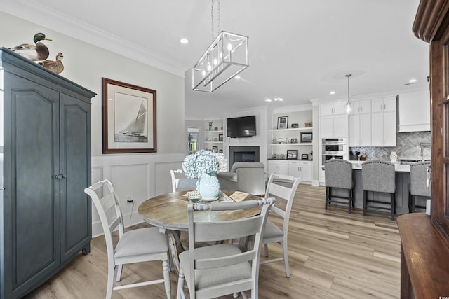 dining room featuring ornamental molding, built in features, an inviting chandelier, and light hardwood / wood-style flooring