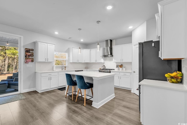 kitchen featuring wall chimney exhaust hood, a breakfast bar, white cabinetry, decorative light fixtures, and a kitchen island