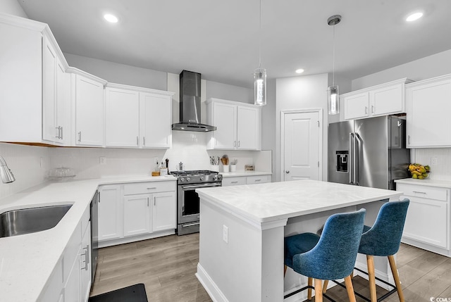 kitchen with wall chimney range hood, sink, stainless steel appliances, a center island, and decorative light fixtures