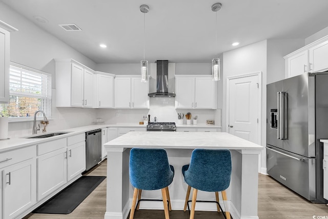 kitchen with appliances with stainless steel finishes, sink, hanging light fixtures, a center island, and wall chimney exhaust hood