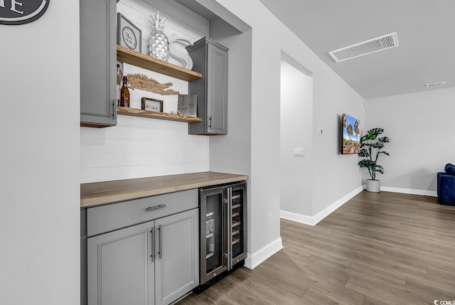 bar with wood counters, gray cabinetry, beverage cooler, and light wood-type flooring