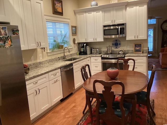 kitchen with sink, appliances with stainless steel finishes, white cabinetry, light stone countertops, and light hardwood / wood-style floors