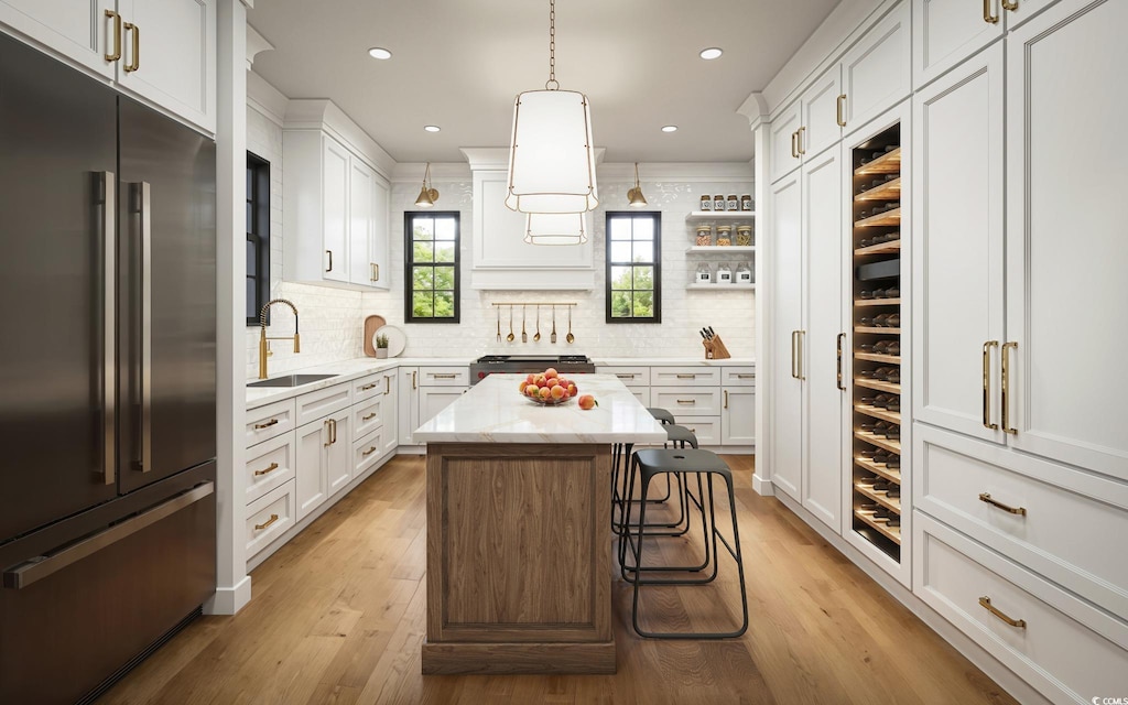 kitchen with sink, built in refrigerator, white cabinetry, a kitchen island, and decorative light fixtures