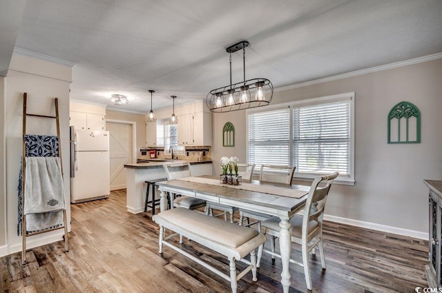 dining area featuring ornamental molding, sink, and light hardwood / wood-style flooring