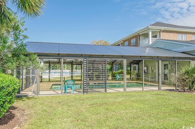 rear view of property with a fenced in pool, a patio, glass enclosure, and a lawn