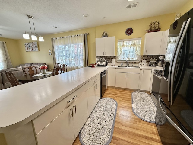 kitchen featuring sink, light hardwood / wood-style flooring, black appliances, white cabinets, and decorative light fixtures