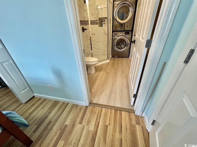 bathroom with tiled shower, stacked washer / drying machine, toilet, and wood-type flooring