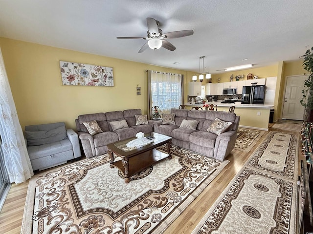 living room with a textured ceiling, ceiling fan, and light hardwood / wood-style flooring