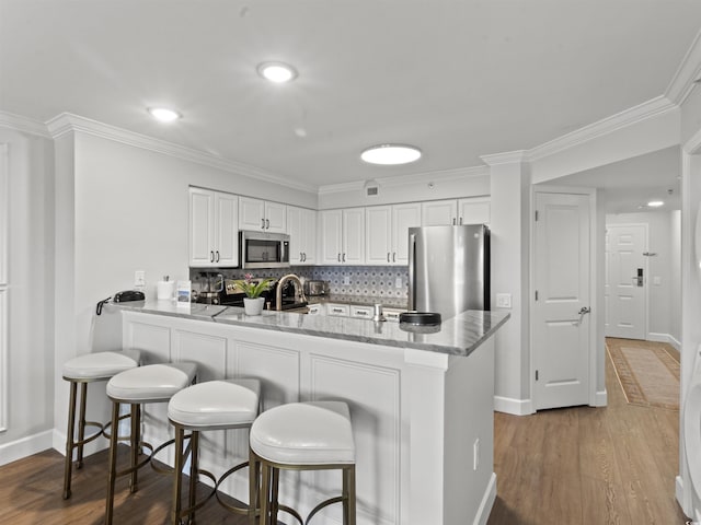 kitchen featuring backsplash, white cabinetry, stainless steel appliances, a breakfast bar area, and dark wood-style flooring