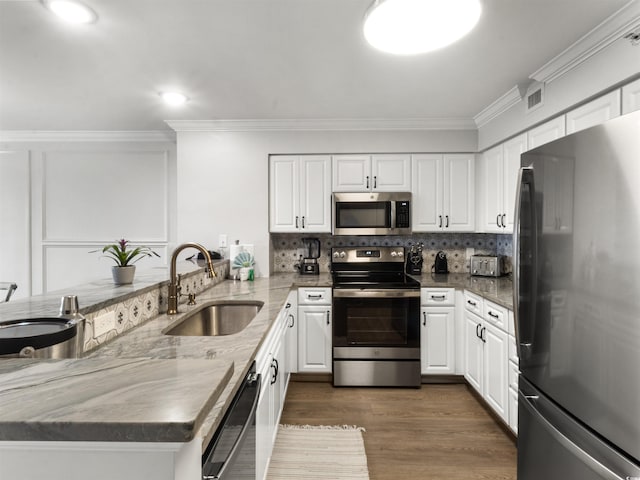 kitchen with a sink, stainless steel appliances, a peninsula, and ornamental molding