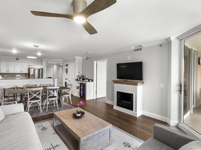 living area featuring wood finished floors, a ceiling fan, stacked washer / drying machine, and ornamental molding