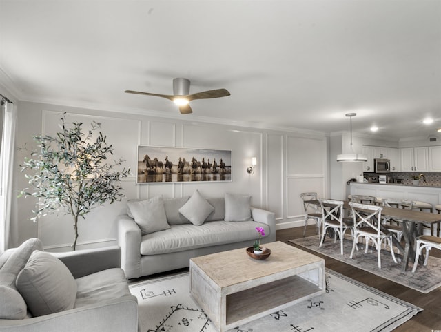 living area featuring ceiling fan, a decorative wall, wood finished floors, and ornamental molding