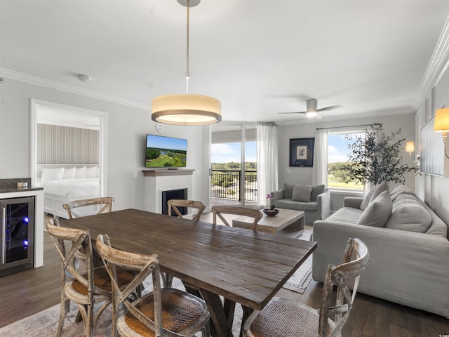 dining space featuring wine cooler, a fireplace, wood finished floors, and crown molding