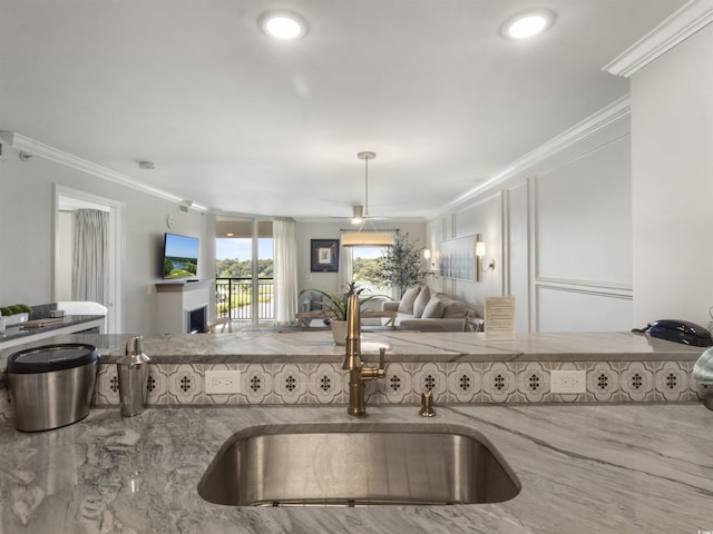 kitchen with open floor plan, ornamental molding, stone counters, and a sink