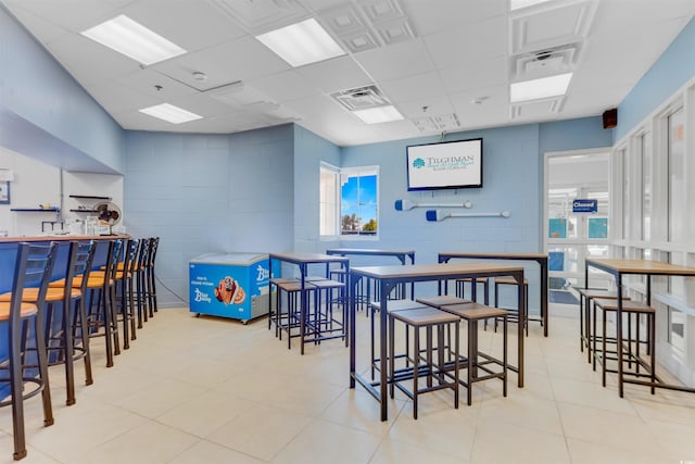 dining room with concrete block wall, visible vents, and a drop ceiling