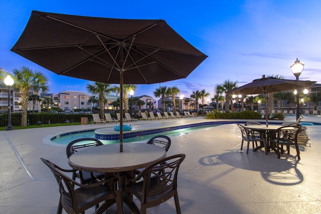 pool at dusk with a community pool, a patio, and fence