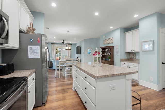 kitchen featuring appliances with stainless steel finishes, a kitchen island, decorative light fixtures, white cabinets, and light wood-type flooring